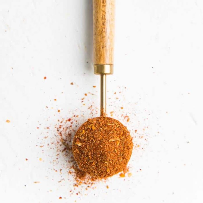 A measuring spoon overfilled with cajun seasoning on a white surface.