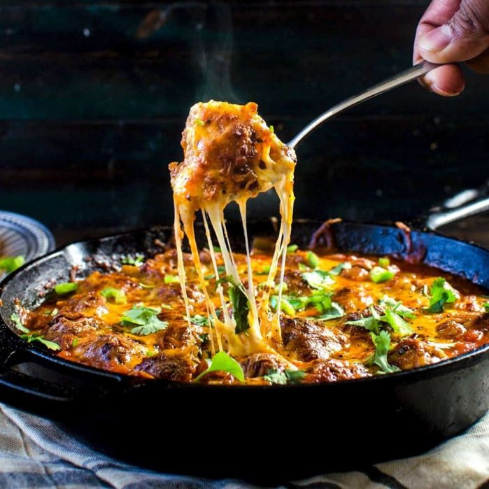 A fork holding up a cheesy meatball over a big Mexican meatball skillet.