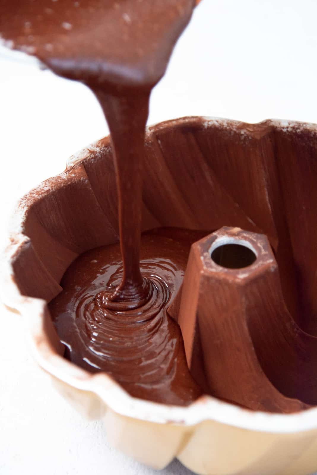 Chocolate cake batter being poured into a prepped bundt cake pan