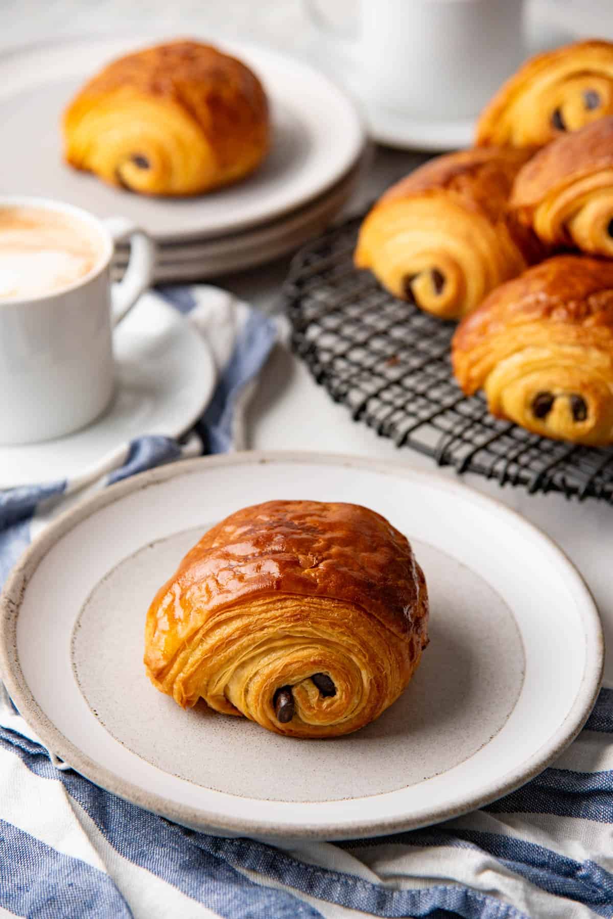 Baked, golden brown chocolate croissant on a white plate, and more croissants in the background.