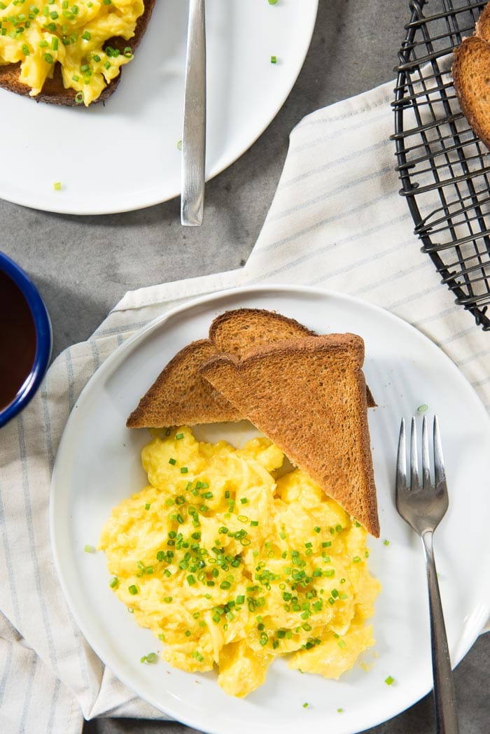 An overhead view of scrambled eggs with chopped chives on top, served on a plate with toast on the side.
