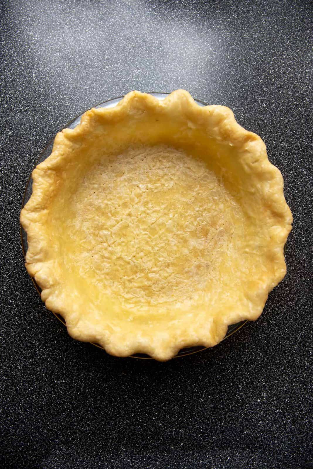 A parbaked pie crust that has a little color all over the pie crust.