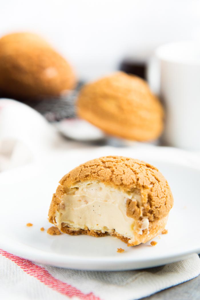 A half eaten choux au craqueline with salted caramel cream filling on a white plate.