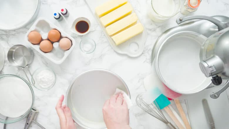 A cake baking station, with a mixer and ingredients and a cake pan being greased.