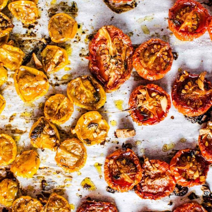 Red and yellow roasted cherry tomatoes sprinkled with olive oil on a parchment paper.