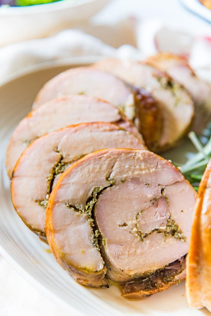 Sliced oven roasted turkey roulade, with a herb rub in the middle, fanned out on a white serving tray.