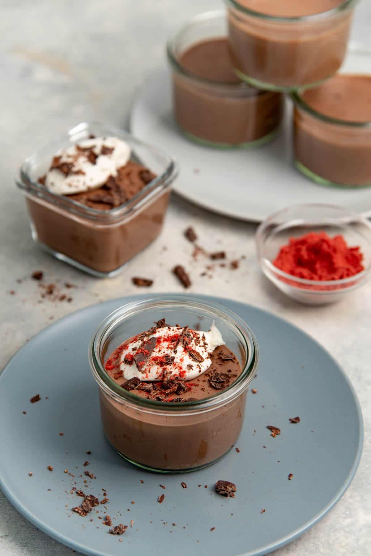 Silken tofu chocolate mousse in a round glass container, topped with whipped cream, chocolate shavings and raspberry powder.